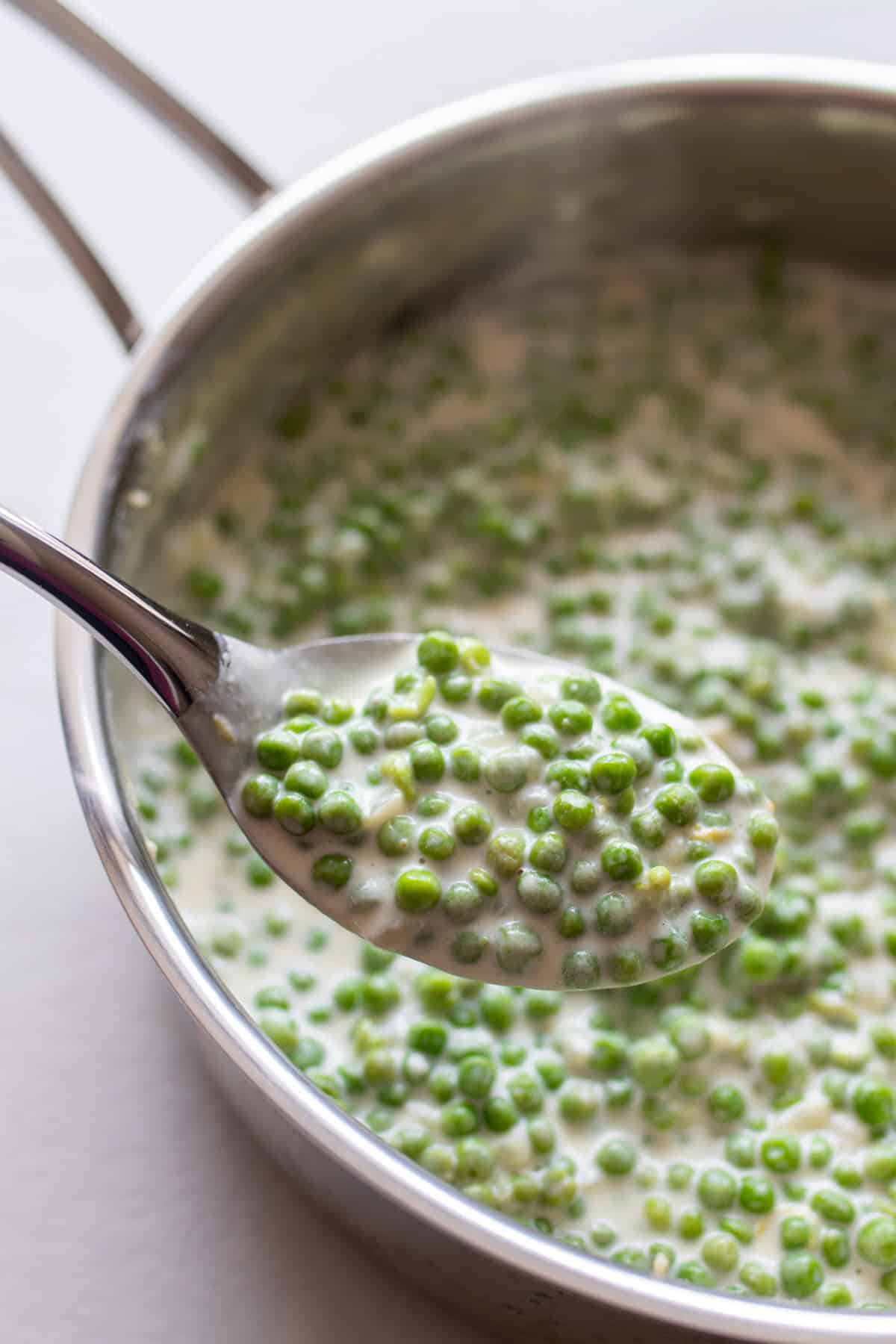 A spoon full of cream peas with a sauce pan of cream peas in the background.