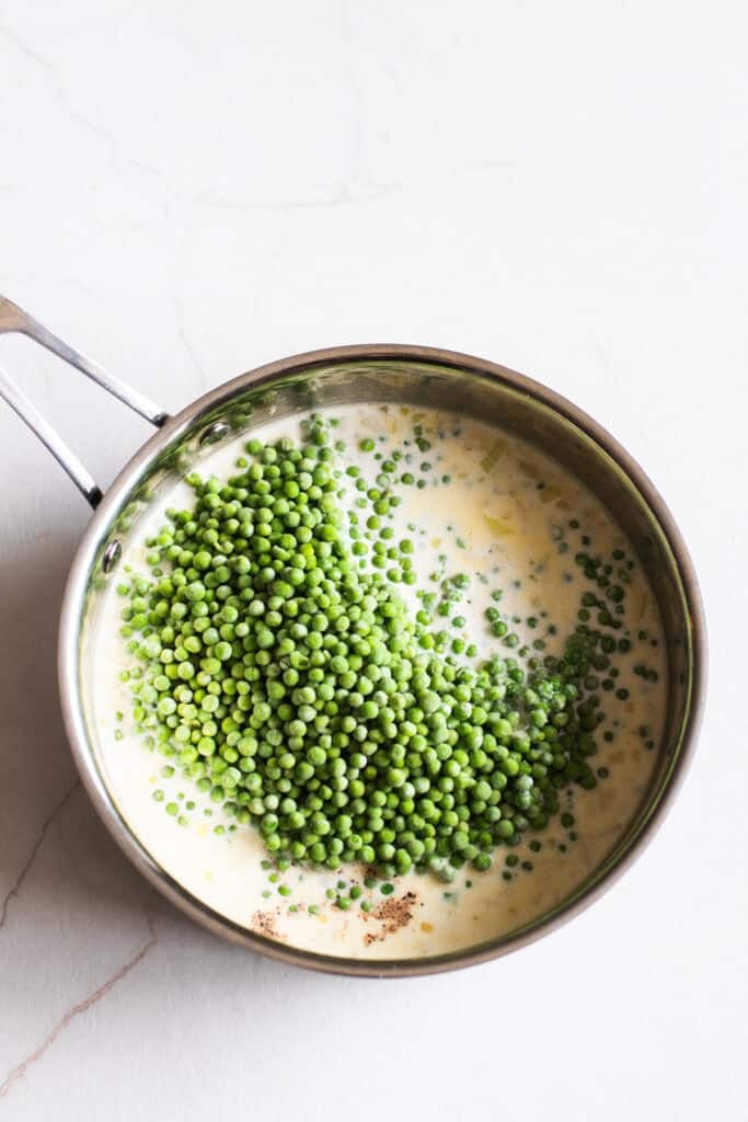 Peas added to a sauce pan full of cream.