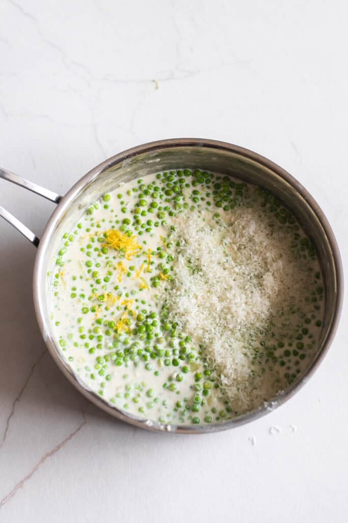 Parmesan added to a sauce pan of peas and cream.