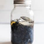 A jar with blueberries and a fermentation weight with a lid on top.