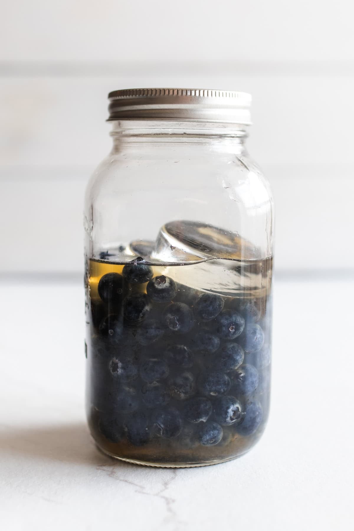 A jar with blueberries and a fermentation weight with a lid on top.