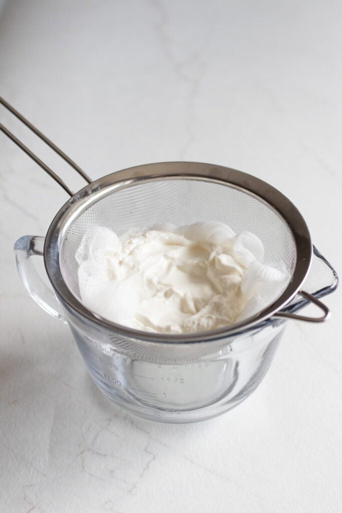 Yogurt in a mesh strainer over a glass bowl. 