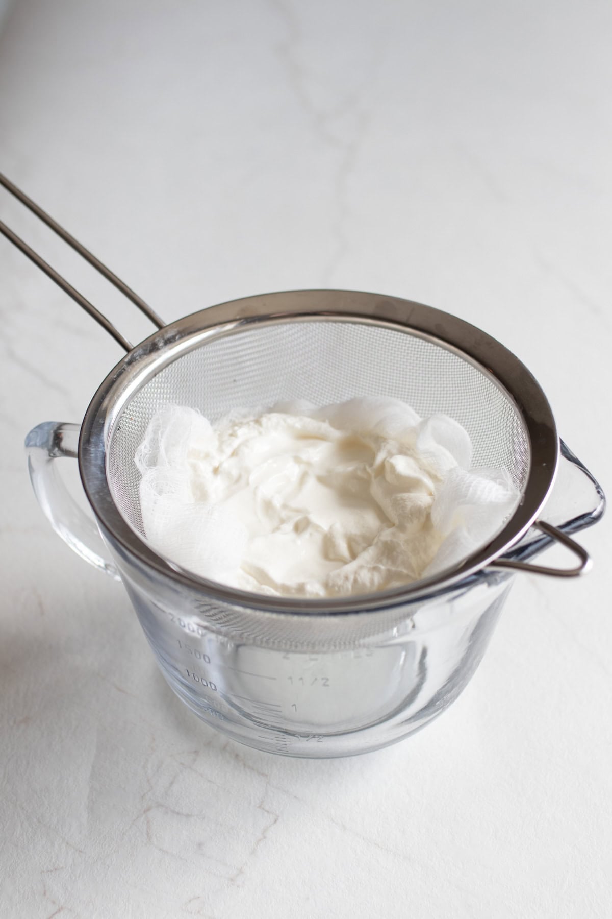 Yogurt in a mesh strainer over a glass bowl.