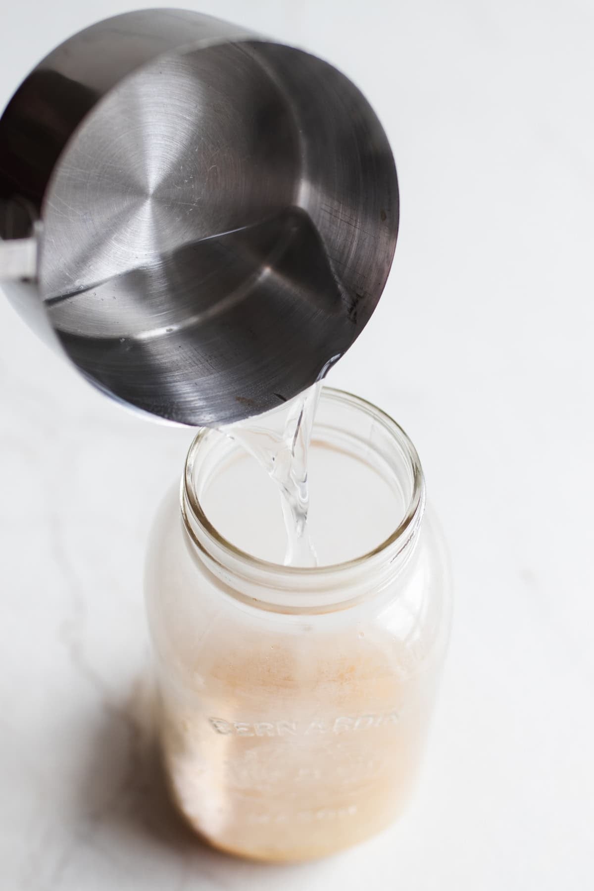 A saucepan of water pouring into a mason jar with salt and sugar on the bottom.