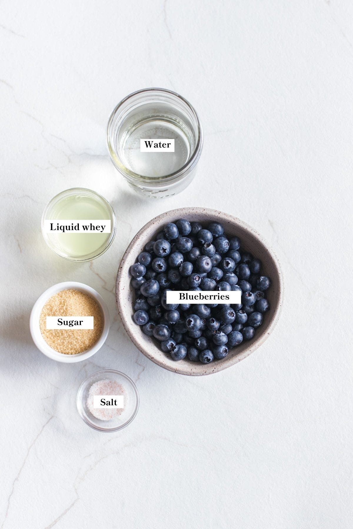 A bowl of blueberries and other ingredients for fermented fruit on a counter top. 