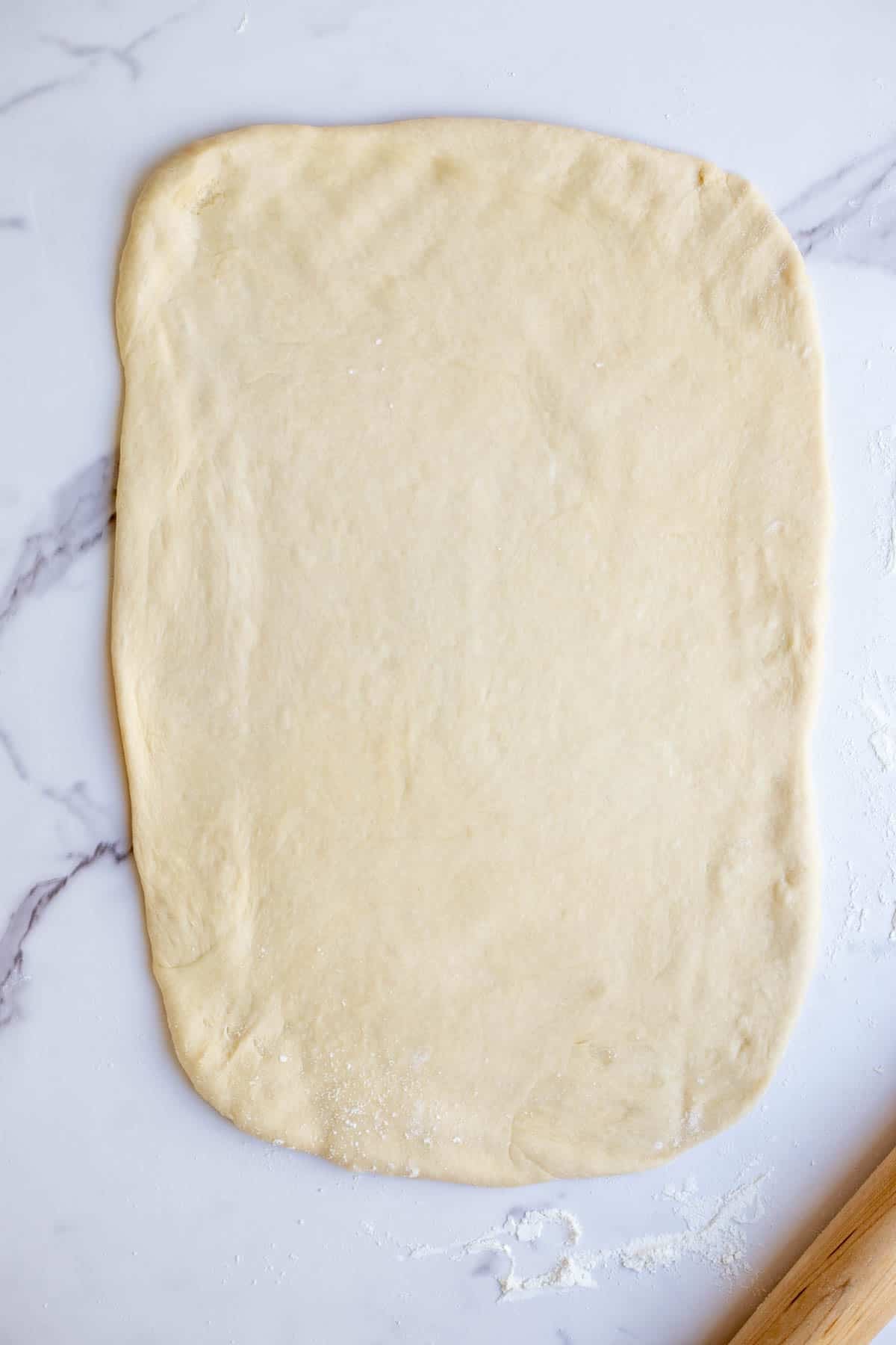 Sourdough rolled out into a rectangle shape on a marble countertop.