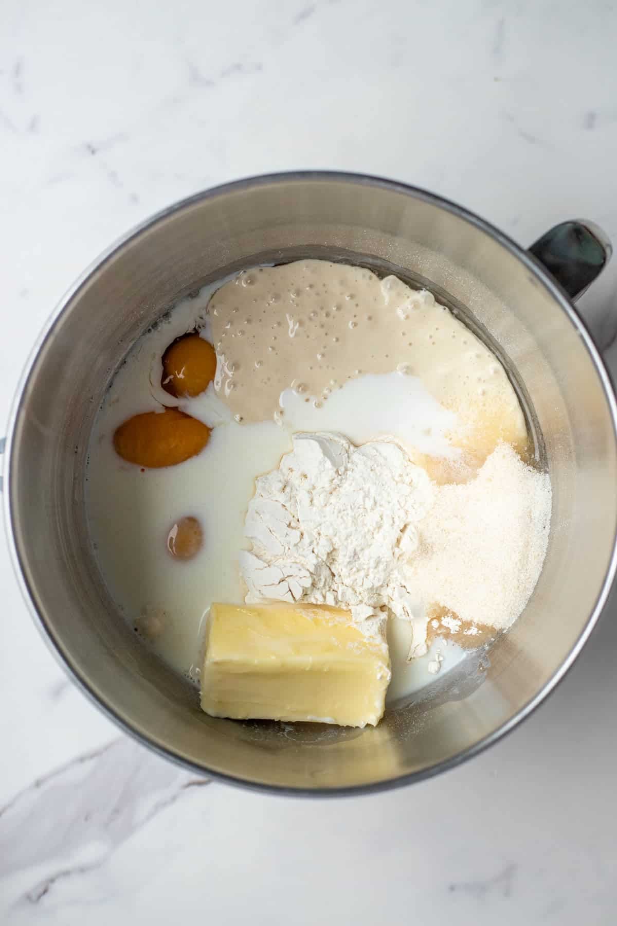 Butter, flour, eggs, sourdough starter, and sugar in a stainless steel mixing bowl.