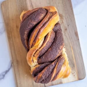 a loaf of sourdough babka placed on a wooden cutting board on a marble counter top.
