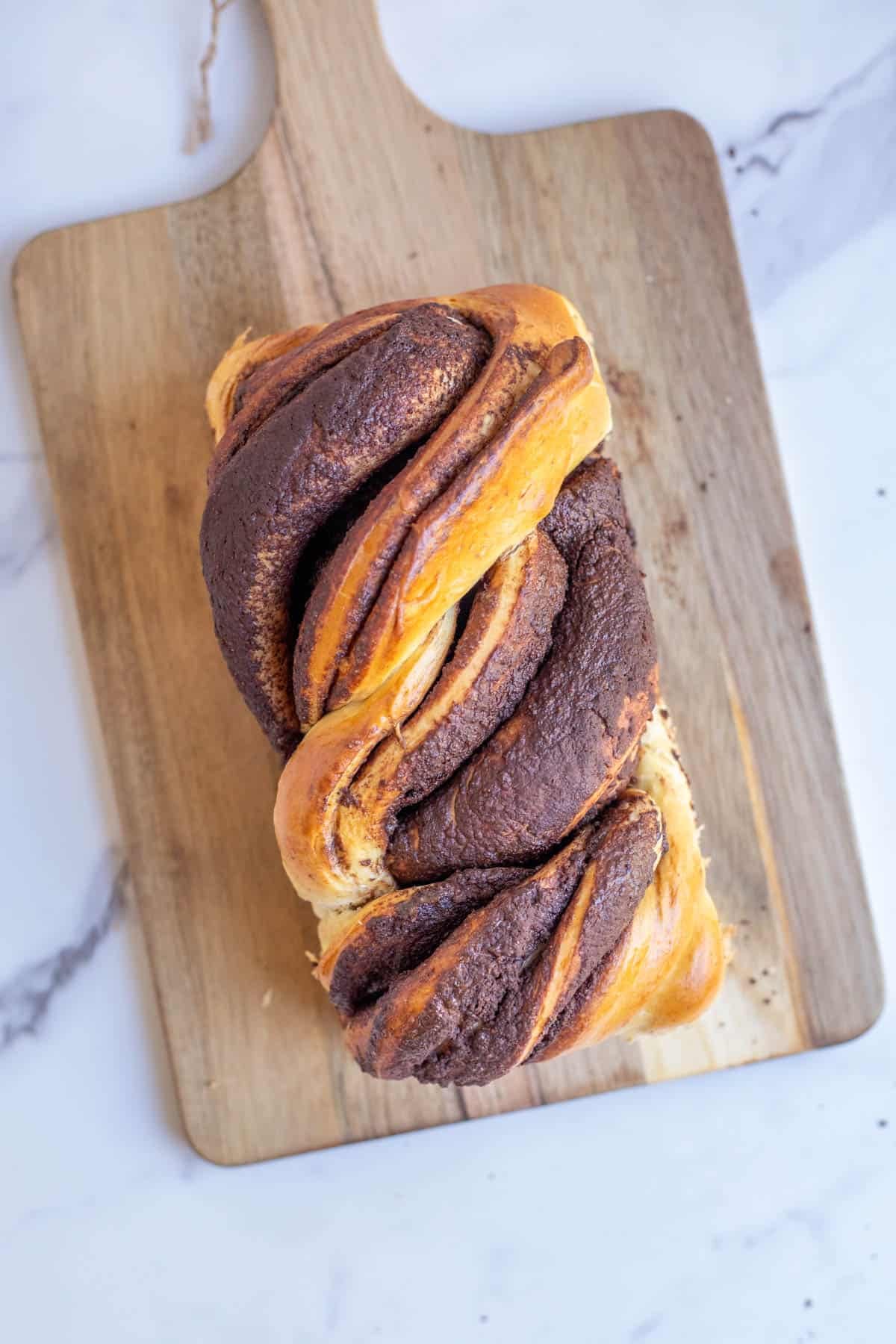 A loaf of sourdough babka placed on a wooden cutting board on a marble counter top.
