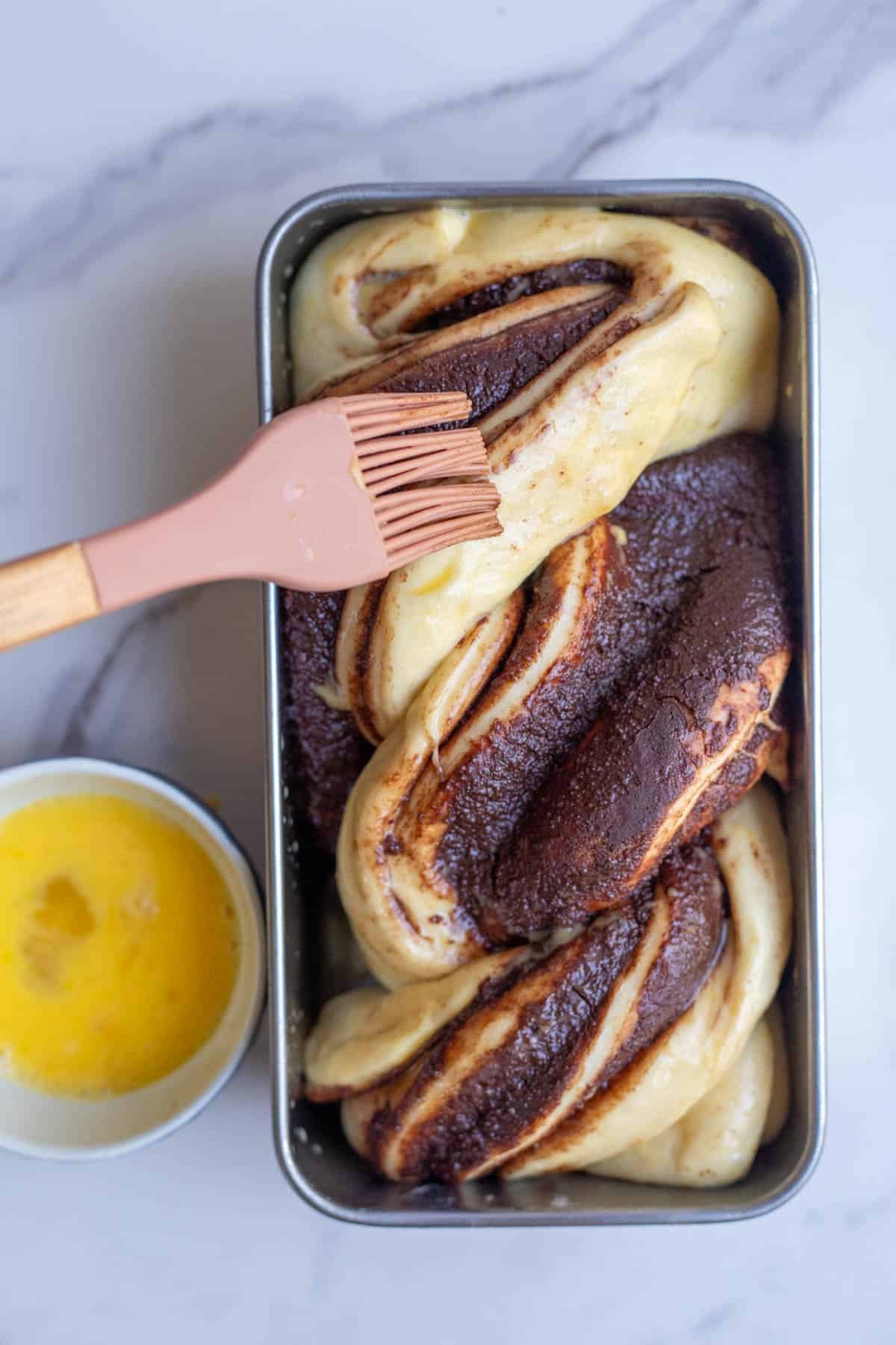 A silicone pastry brush applying an egg wash to the sourdough babka dough. 