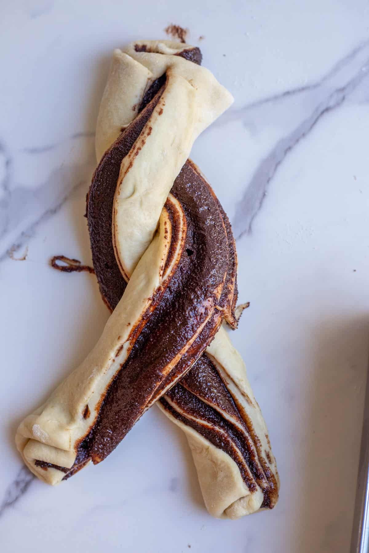 Split babka dough twisted together on a marble countertop. 
