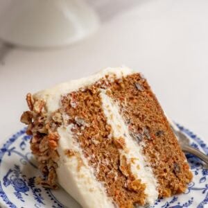 a slice of sourdough carrot cake iced with cream cheese frosting on a blue decorative plate.