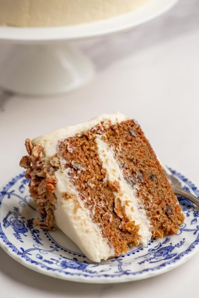a slice of sourdough carrot cake iced with cream cheese frosting on a blue decorative plate.
