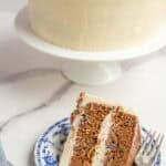 a slice of sourdough carrot cake on a blue dessert plate with the remaining cake in the background.