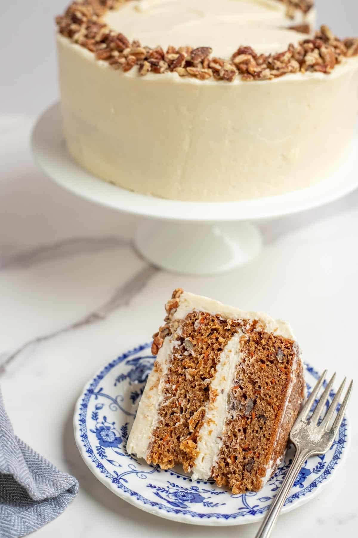 a slice of sourdough carrot cake on a blue dessert plate with the remaining cake in the background.