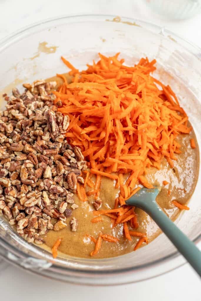 dry and wet cake ingredients mixed together with pecans and shredded carrots on top of the batter.