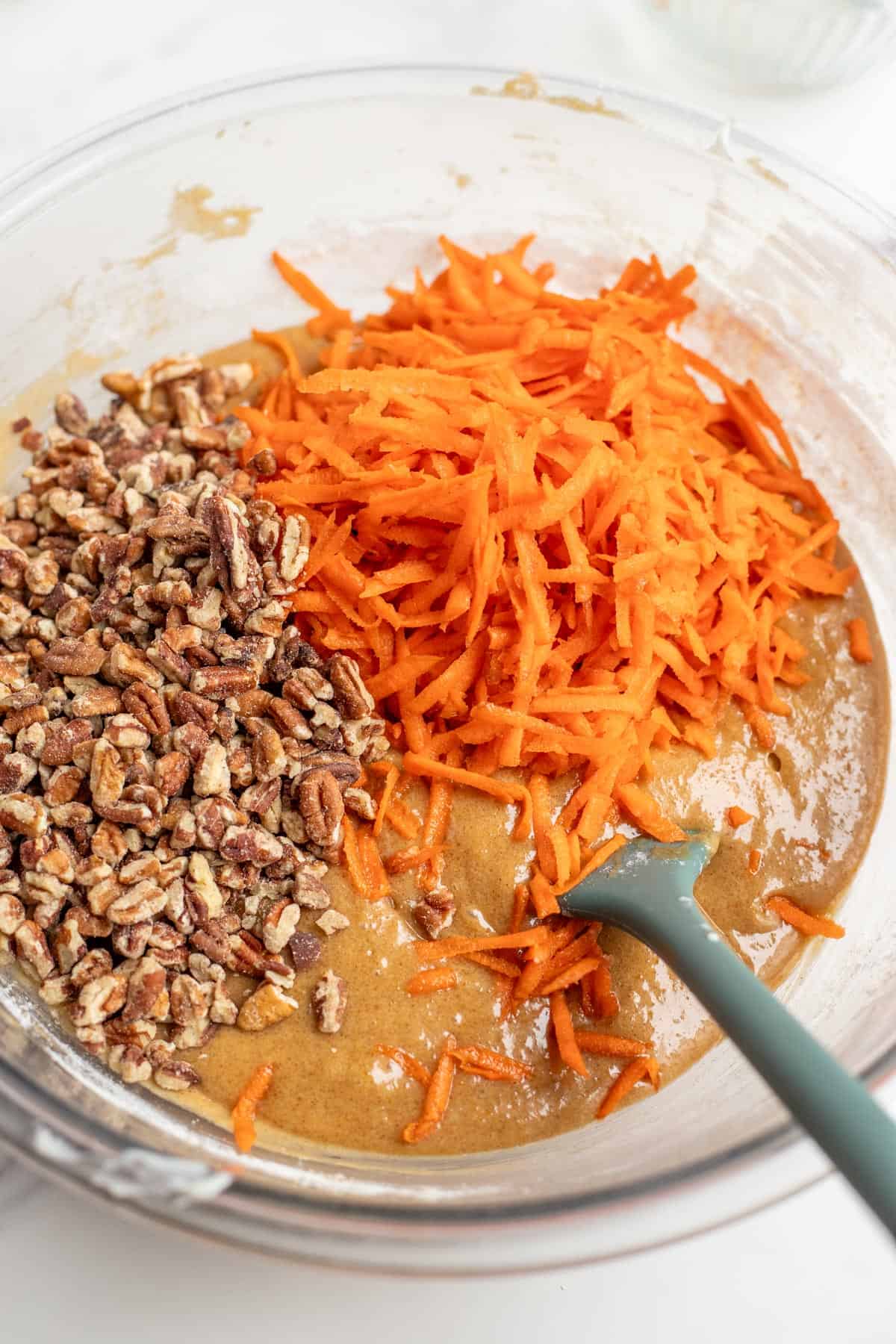 dry and wet cake ingredients mixed together with pecans and shredded carrots on top of the batter.