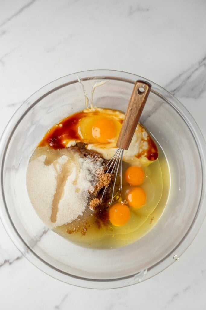 eggs, sugar, vanilla, and sourdough starter in a glass bowl with a metal whisk.