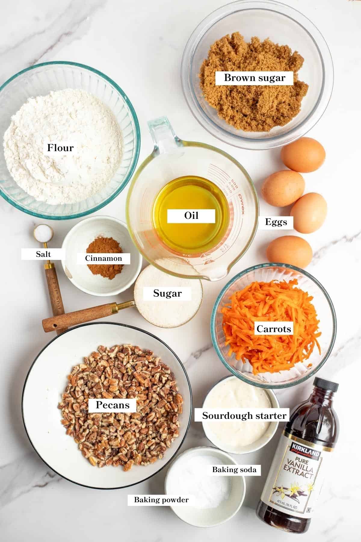 single ingredients in glass bowls on the countertop to make a carrot cake.