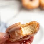 someone holding up a sourdough donut that has one bite out of it.