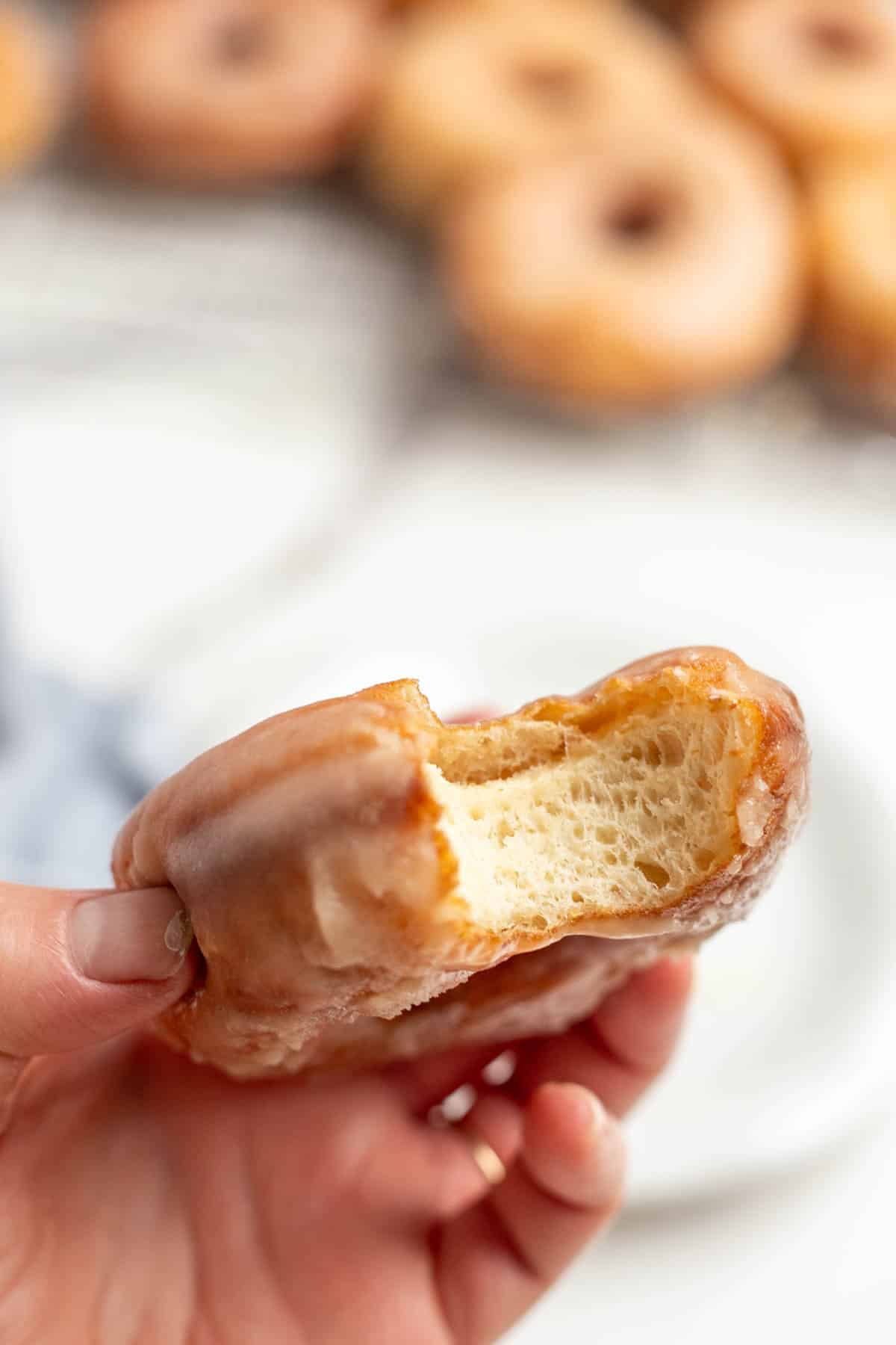 Someone holding up a sourdough donut that has one bite out of it. 