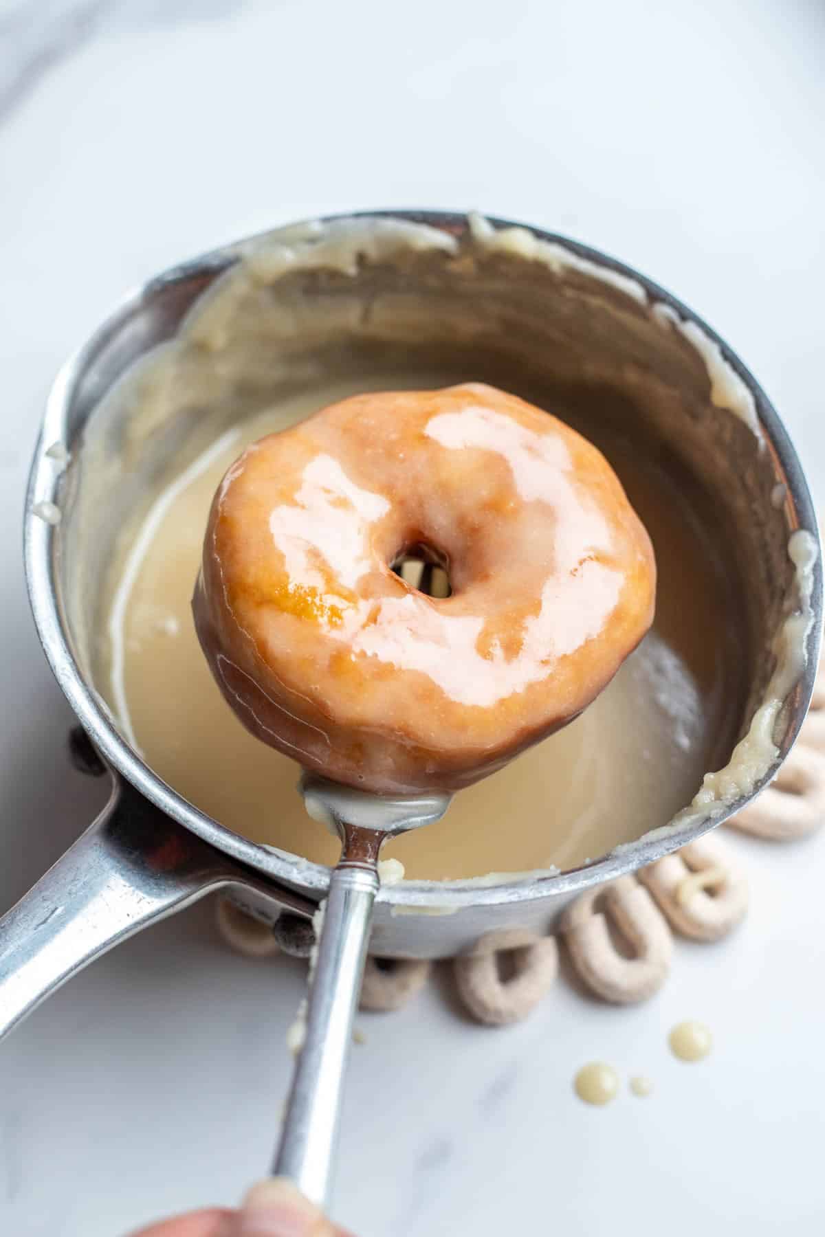 A sourdough donut dipped into a pot of vanilla glaze.