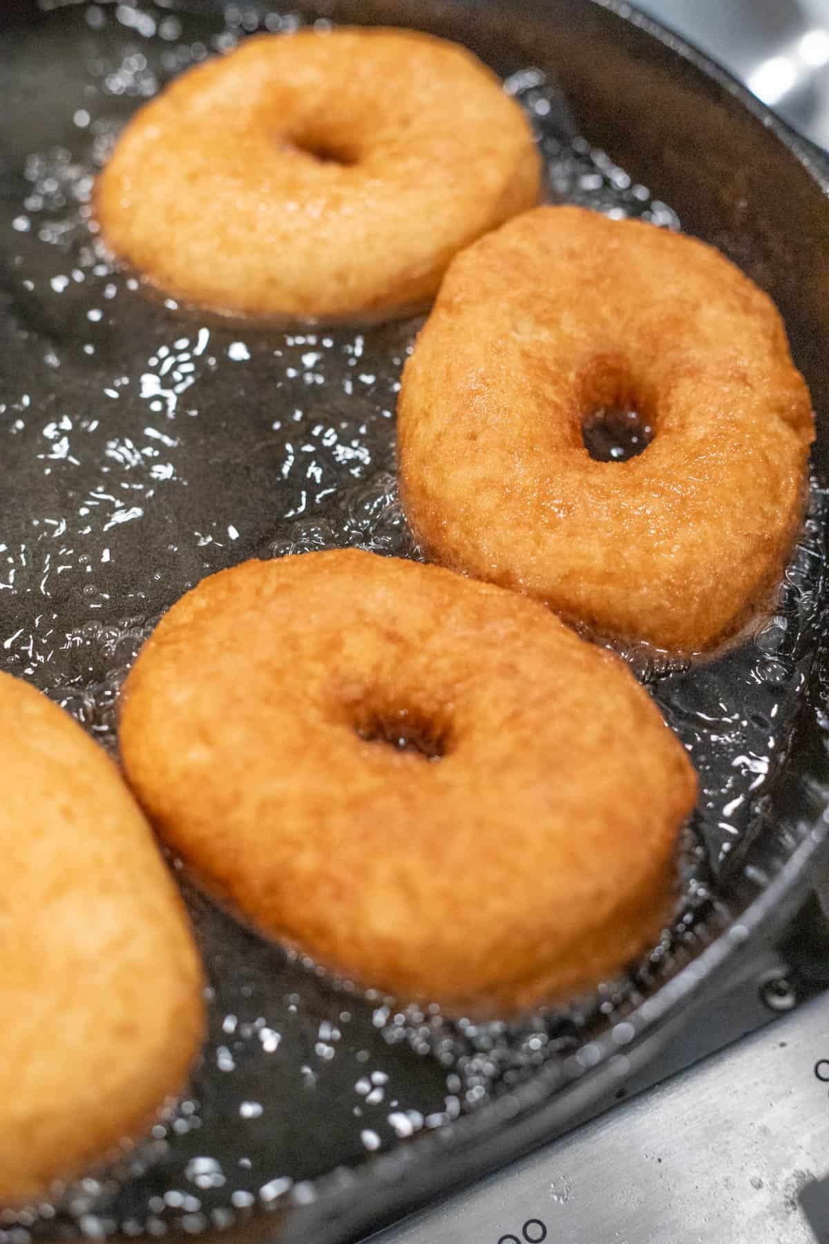 Four donuts frying in a cast iron skillet filled with oil.