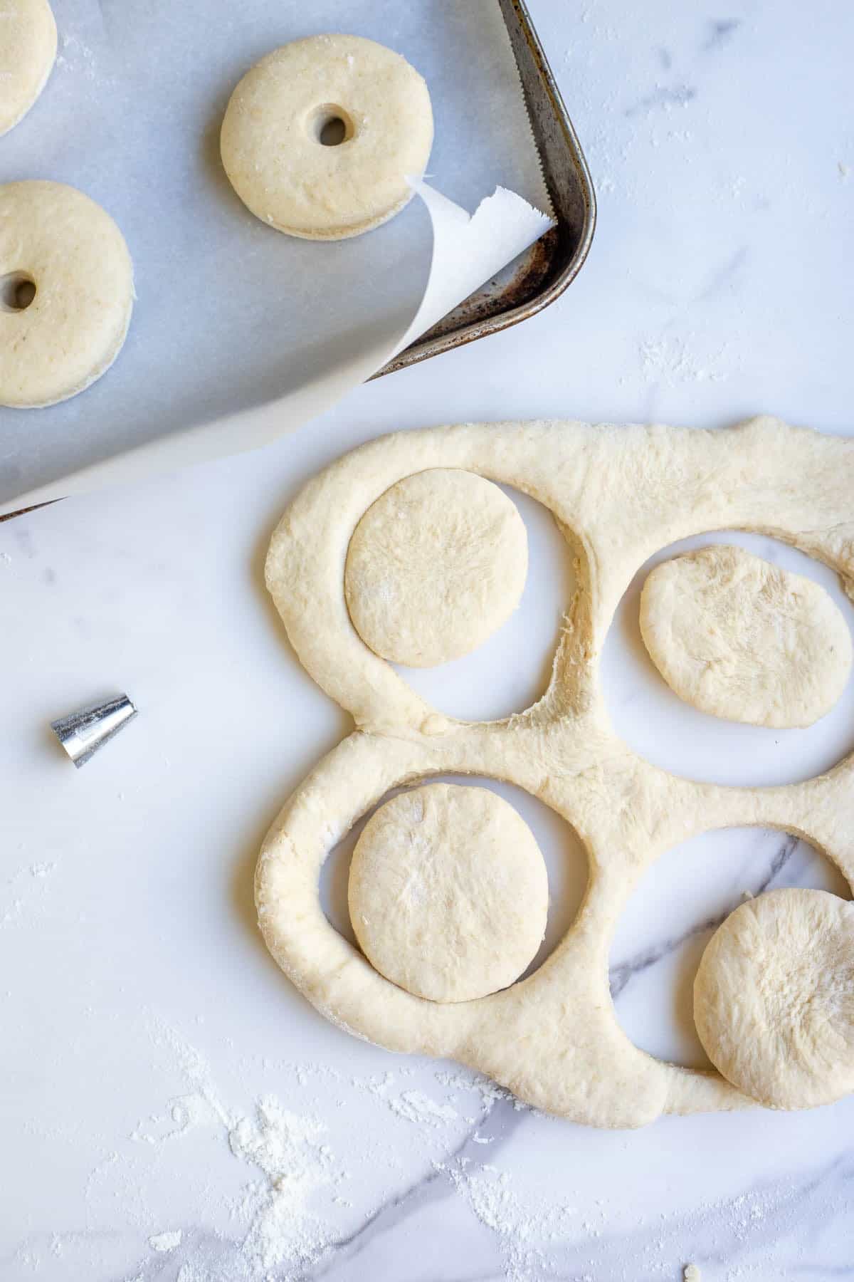 Dough rolled out on a marble countertop with four circles cut out of the dough to make donuts.