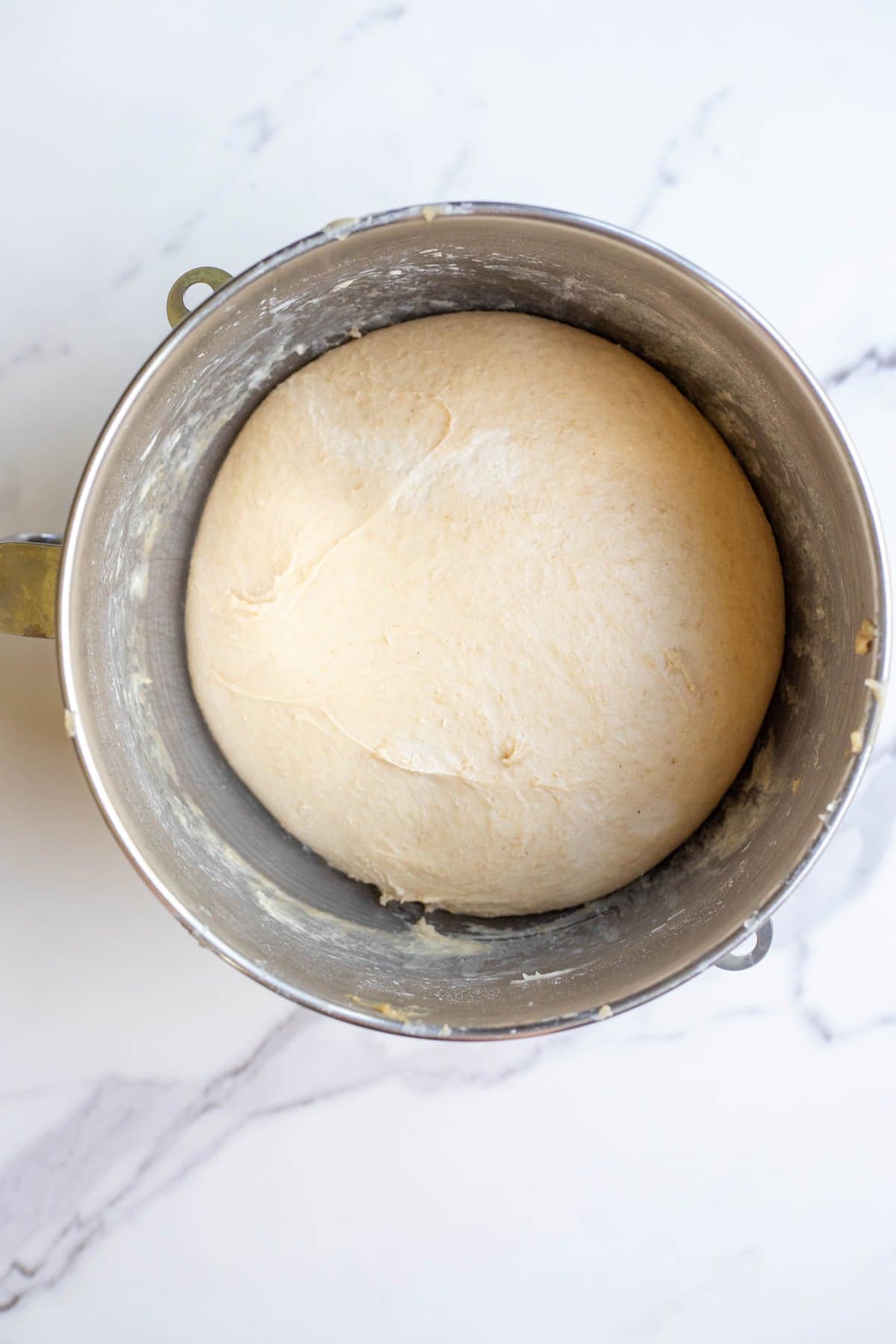 A risen ball of sourdough in a stainless steel mixing bowl on a marble counter.