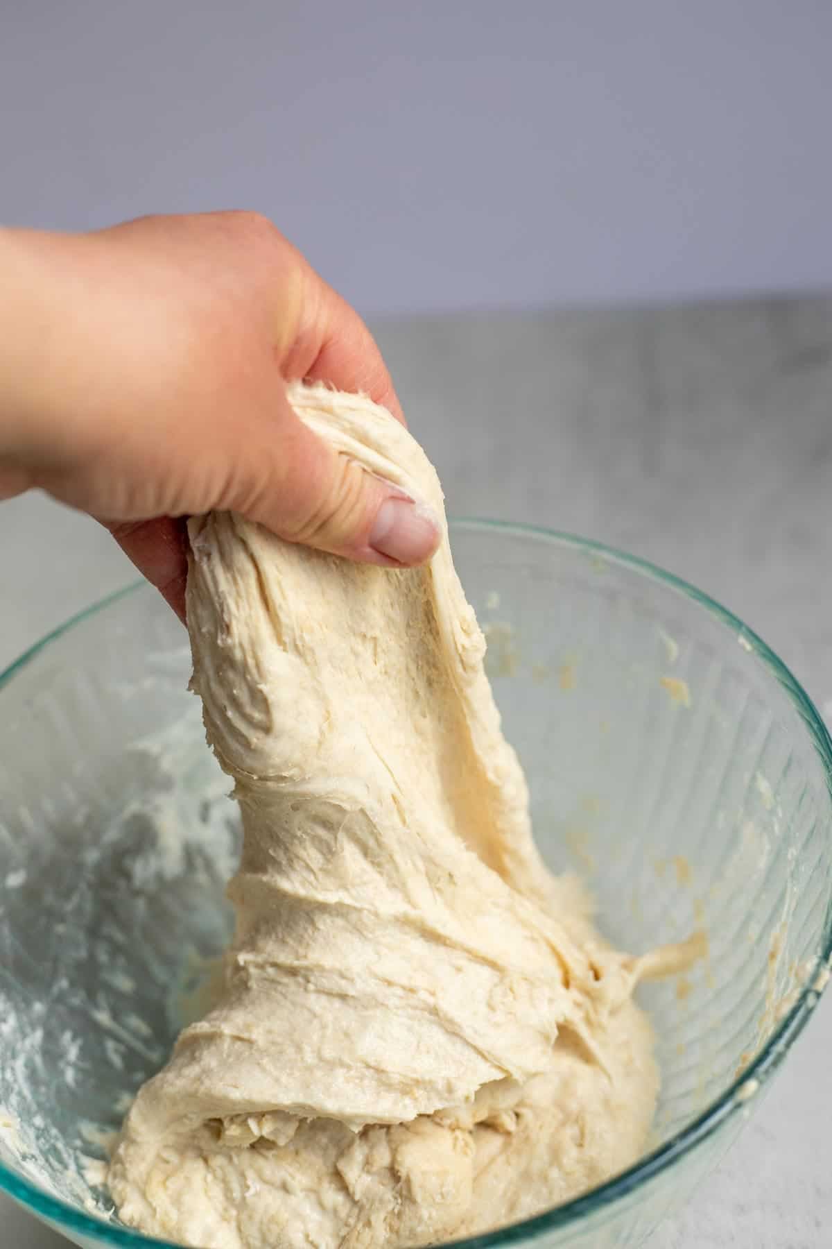 A hand stretching dough out of a bowl.