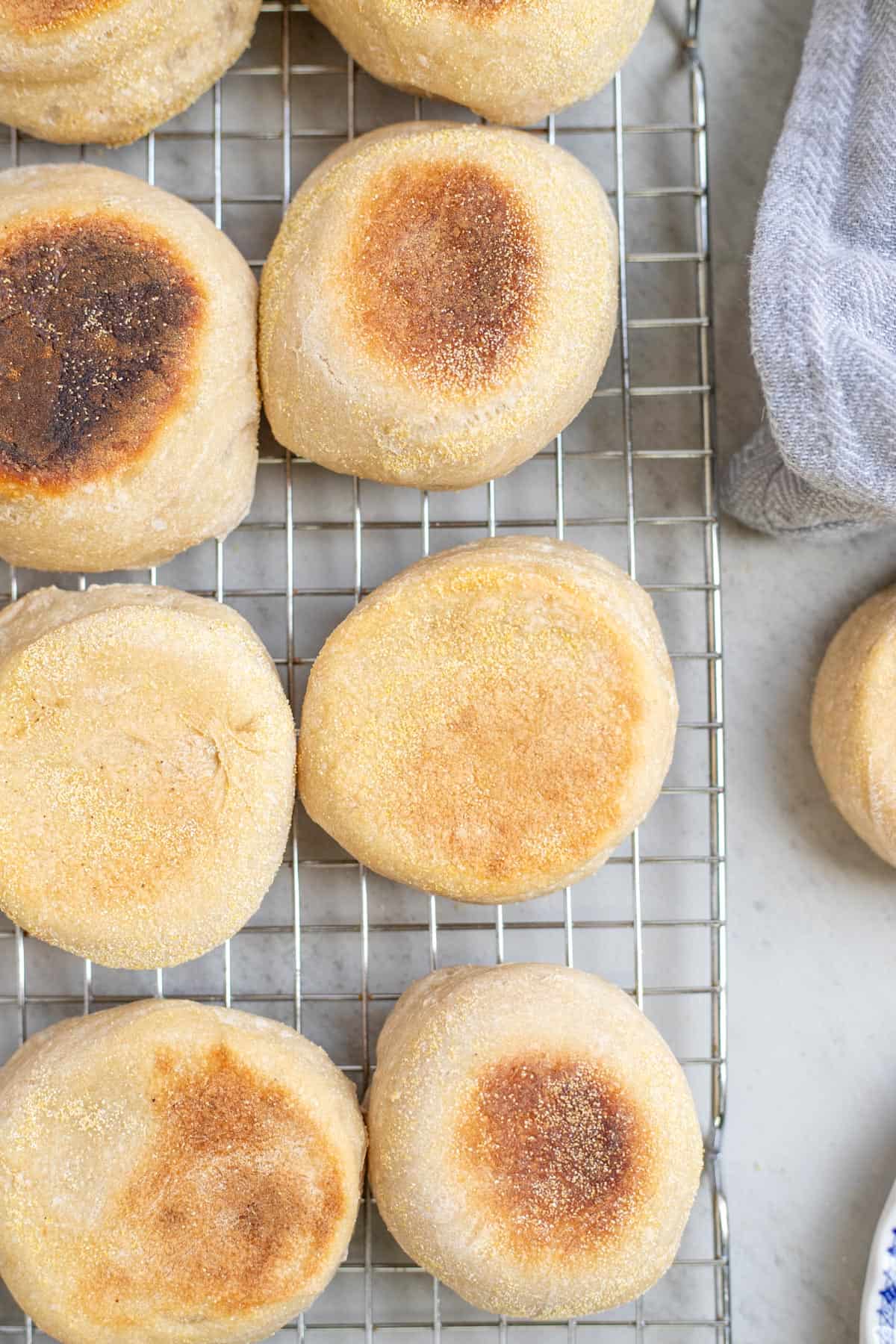 Browned English muffins cooling on a wire rack on the kitchen counter.