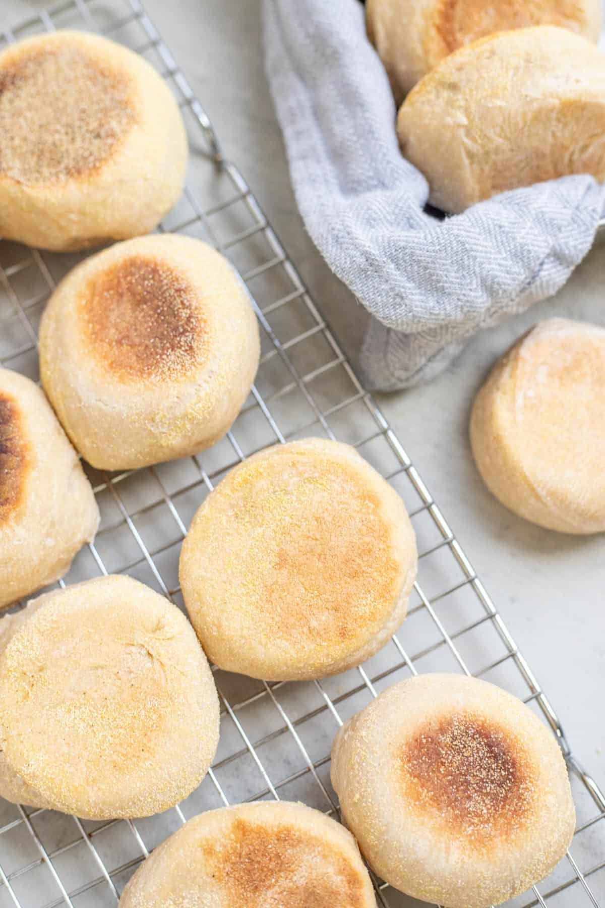 Browned English muffins cooling on a wire rack on the kitchen counter.