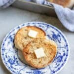 an english muffin split open with a pad of butter on each side of the muffin on a blue decorative plate.
