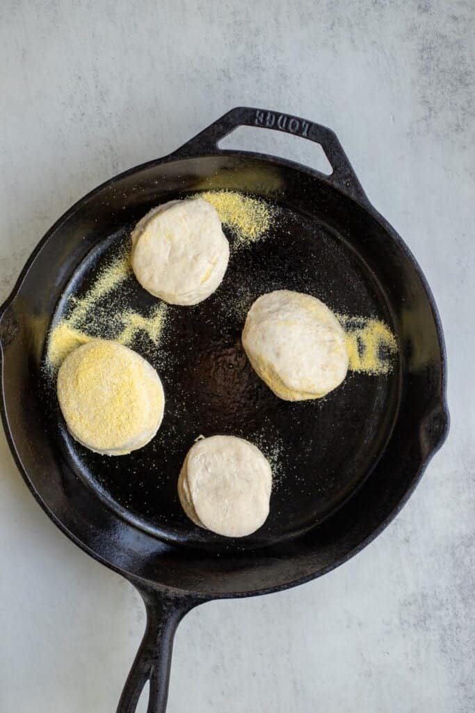 Four English muffins added to a greased cast iron skillet.