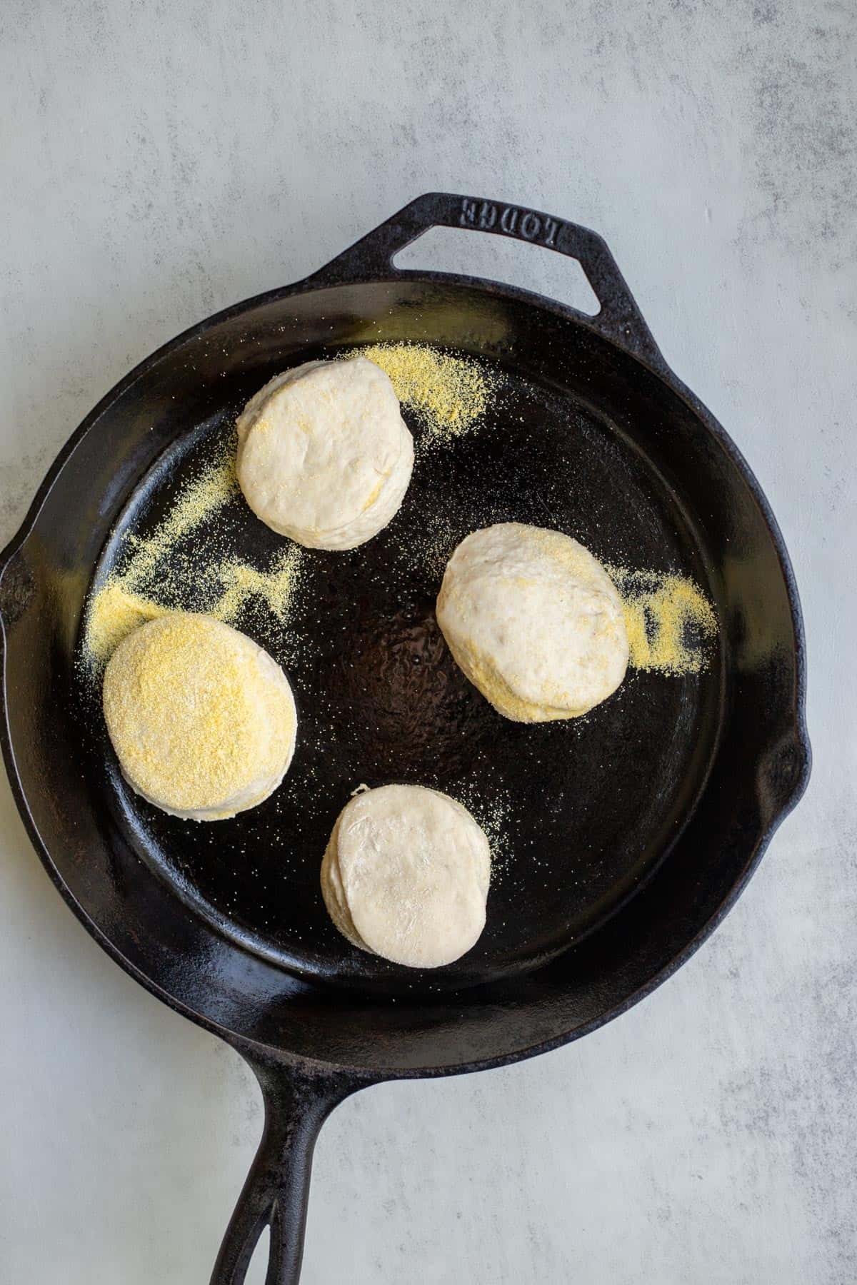 Four English muffins added to a greased cast iron skillet.