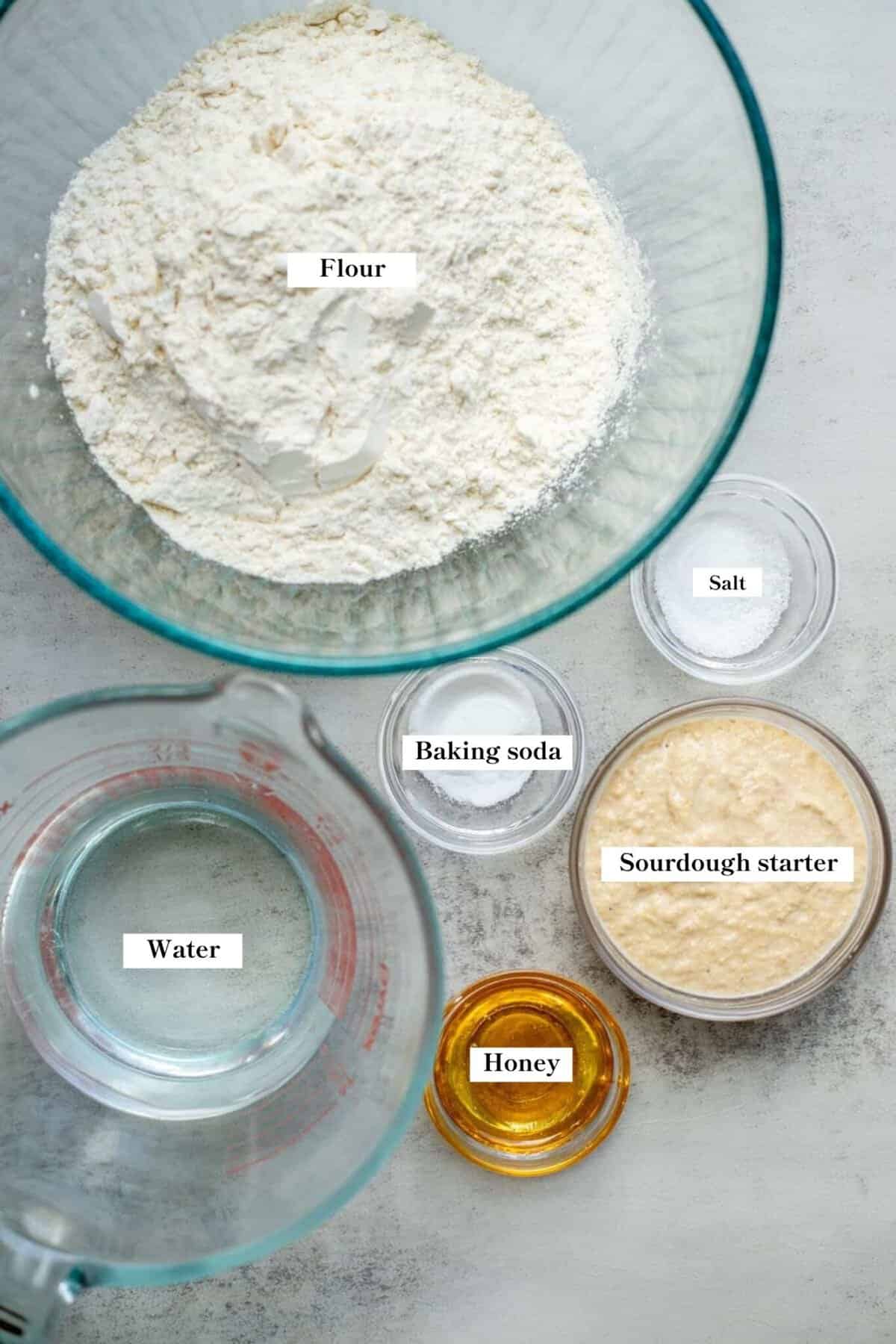 Ingredients for sourdough English muffins in small glass bowls on the counter.