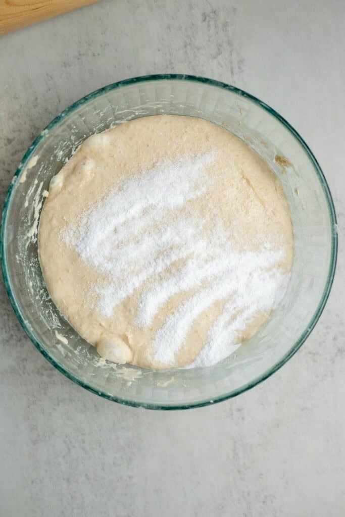 Baking soda sprinkled on top of a sourdough English muffin dough in a glass bowl.