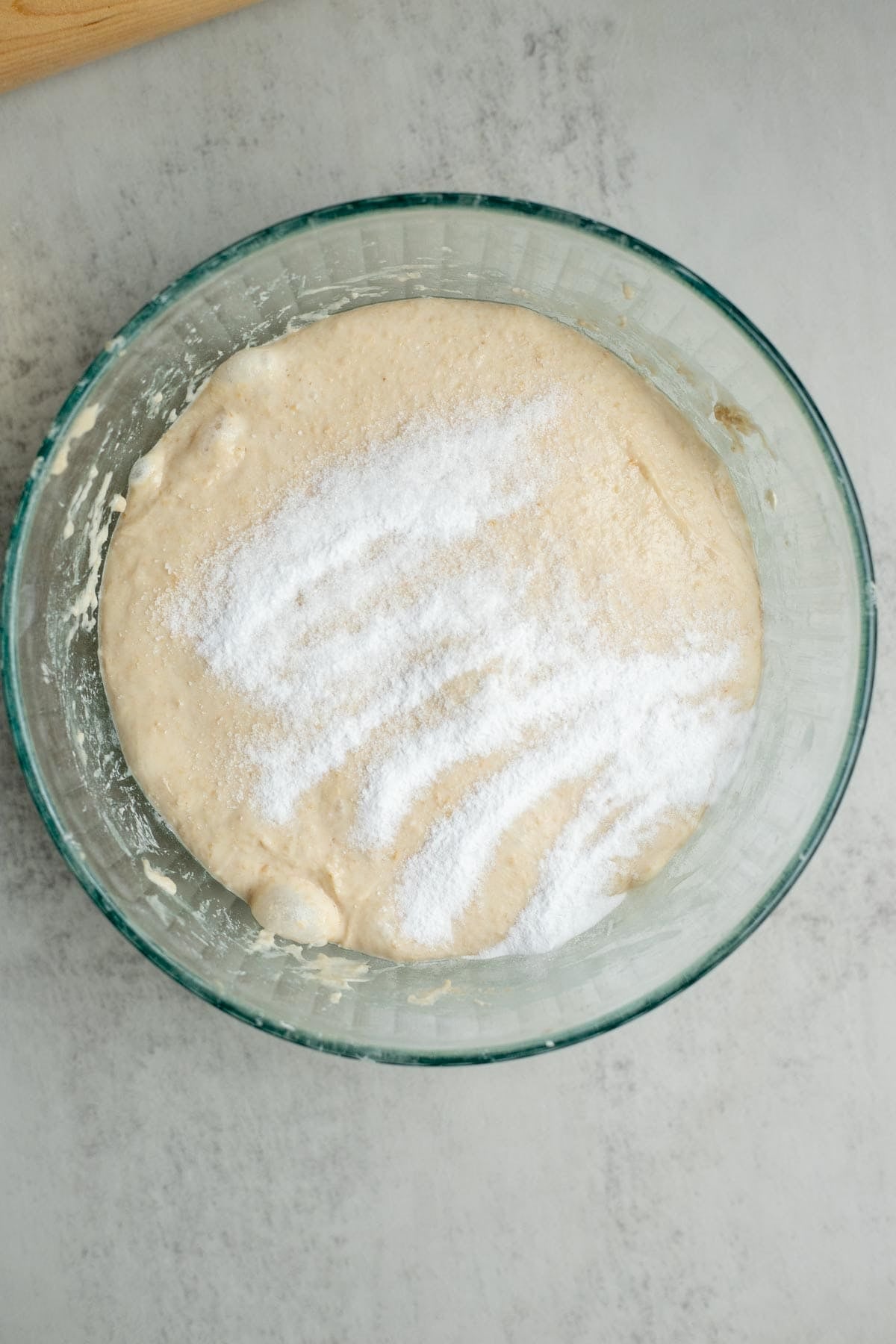 Baking soda sprinkled on top of a sourdough English muffin dough in a glass bowl.