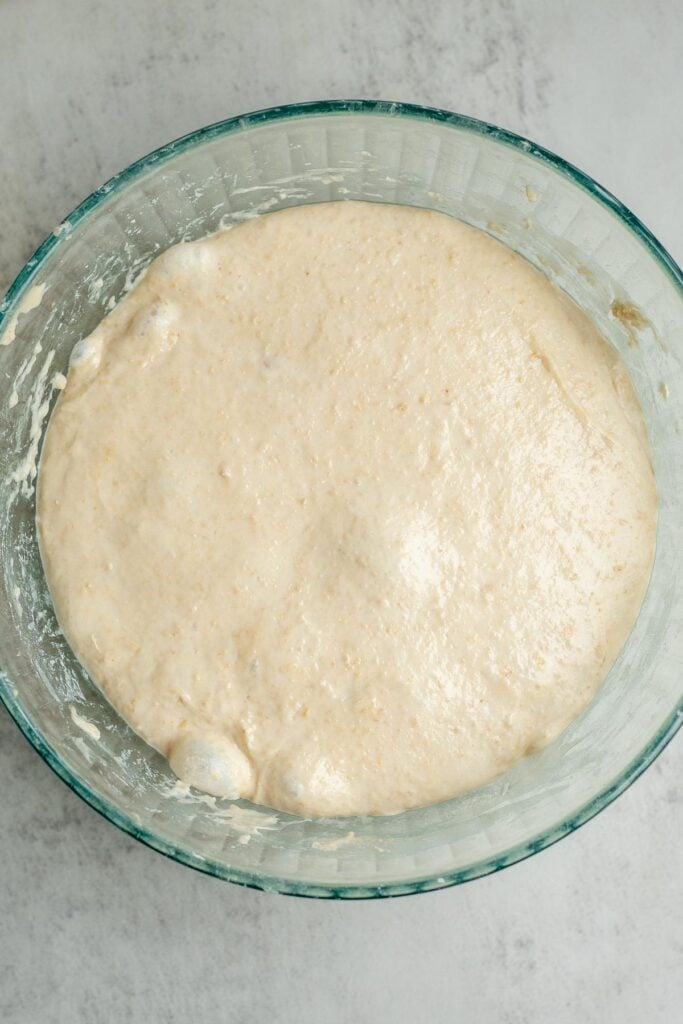Sourdough English muffin dough doubled in size and fermenting in a glass bowl.