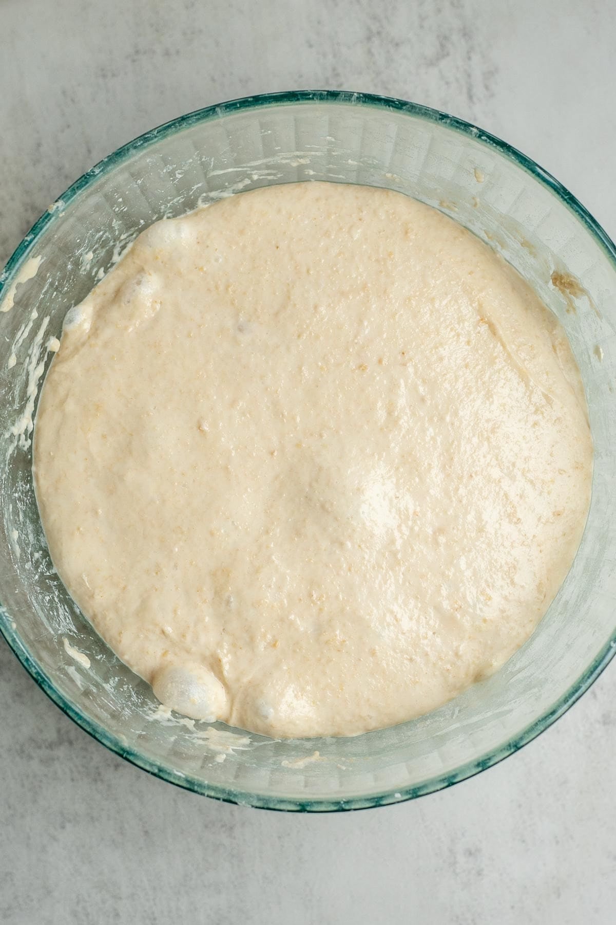 Sourdough English muffin dough doubled in size and fermenting in a glass bowl.