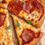 A pepperoni pizza on a wooden cutting board with one slice cut out.