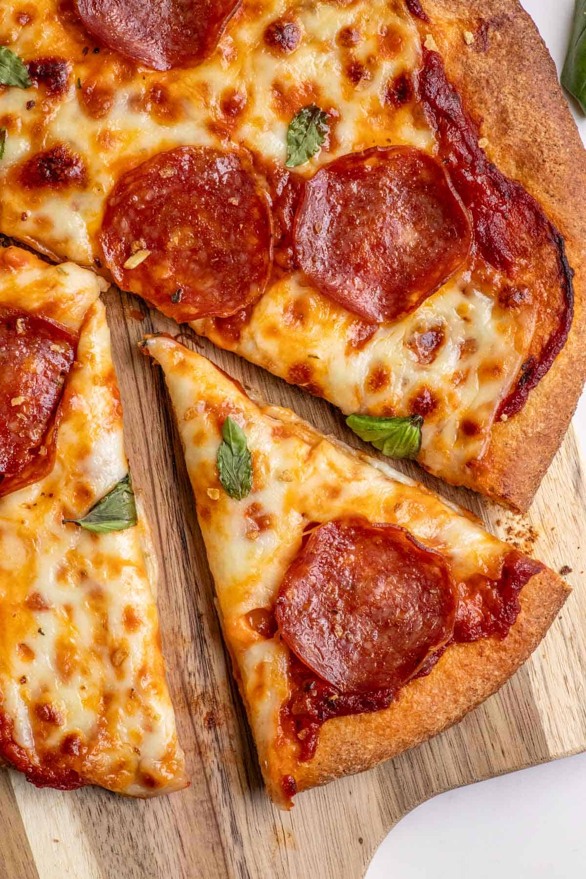 A pepperoni pizza on a wooden cutting board with one slice cut out.