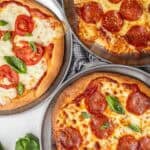 Three different pizzas next to each other on a counter top.