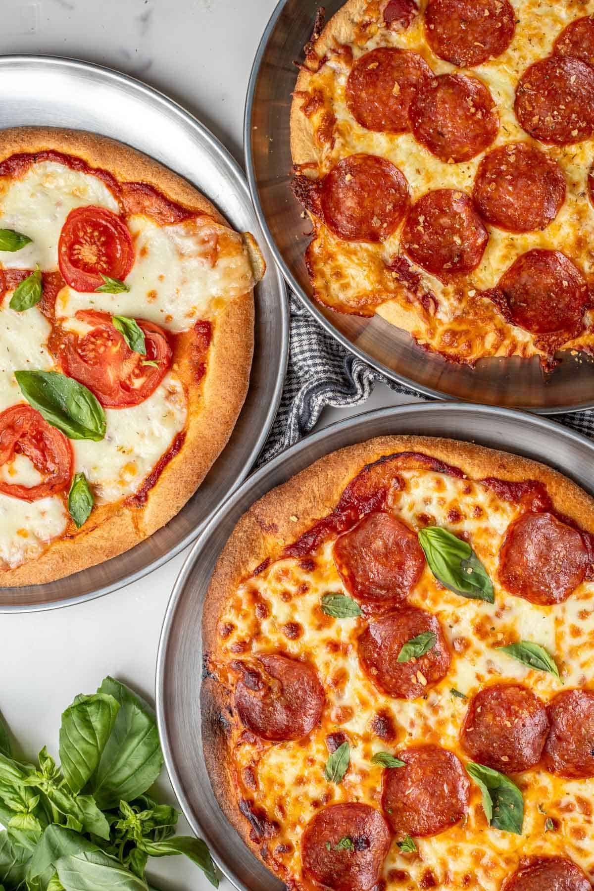 Three different pizzas next to each other on a counter top.