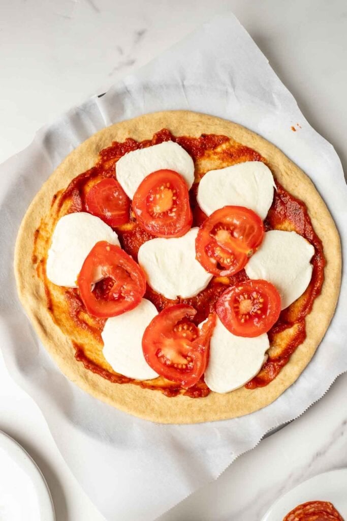 Pizza toppings added to a pizza dough on a pizza pan.