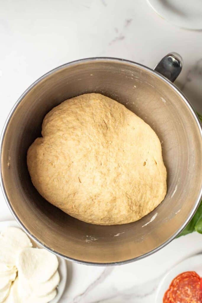 A dough ball doubled in size in a stand mixer bowl after the first rise.