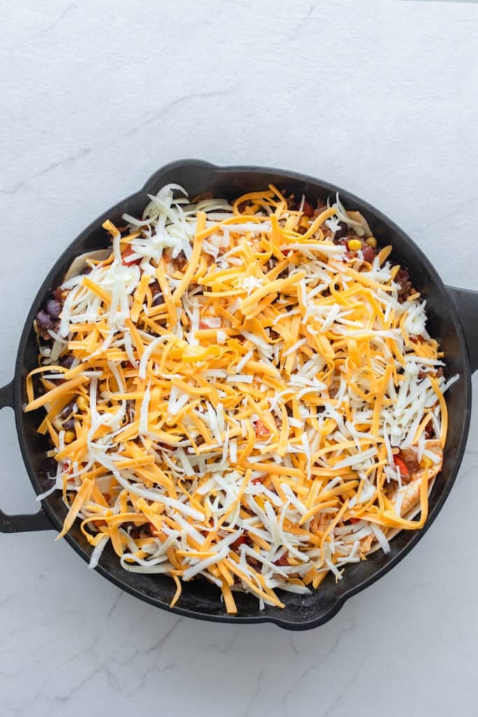 Shredded cheese on top of a ground beef mixture in a cast iron skillet.