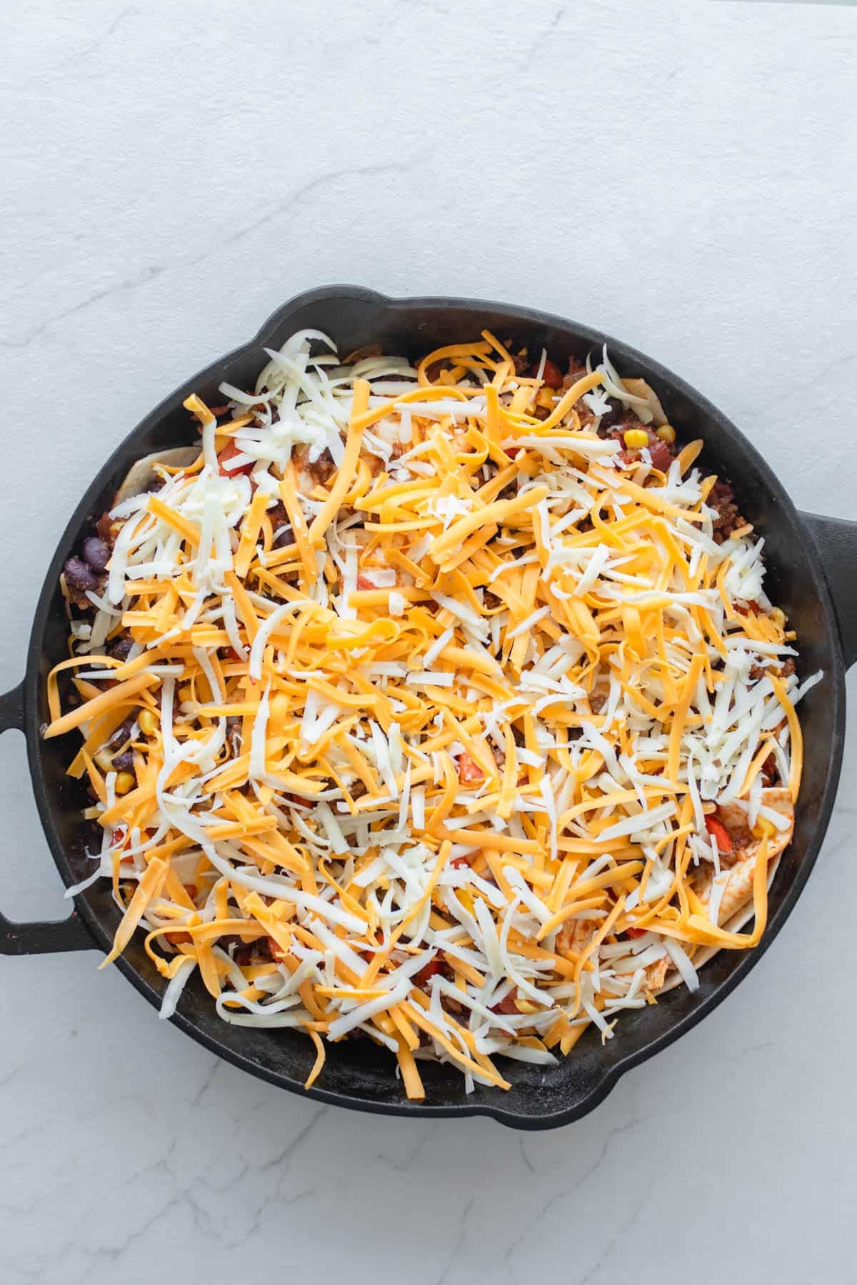 Shredded cheese on top of a ground beef mixture in a cast iron skillet.