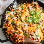 A wooden spoon dishing out some of a taco skillet in a cast iron skillet.