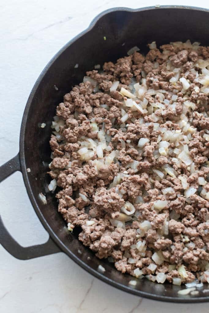 Ground beef and chopped onion in a cast iron skillet.